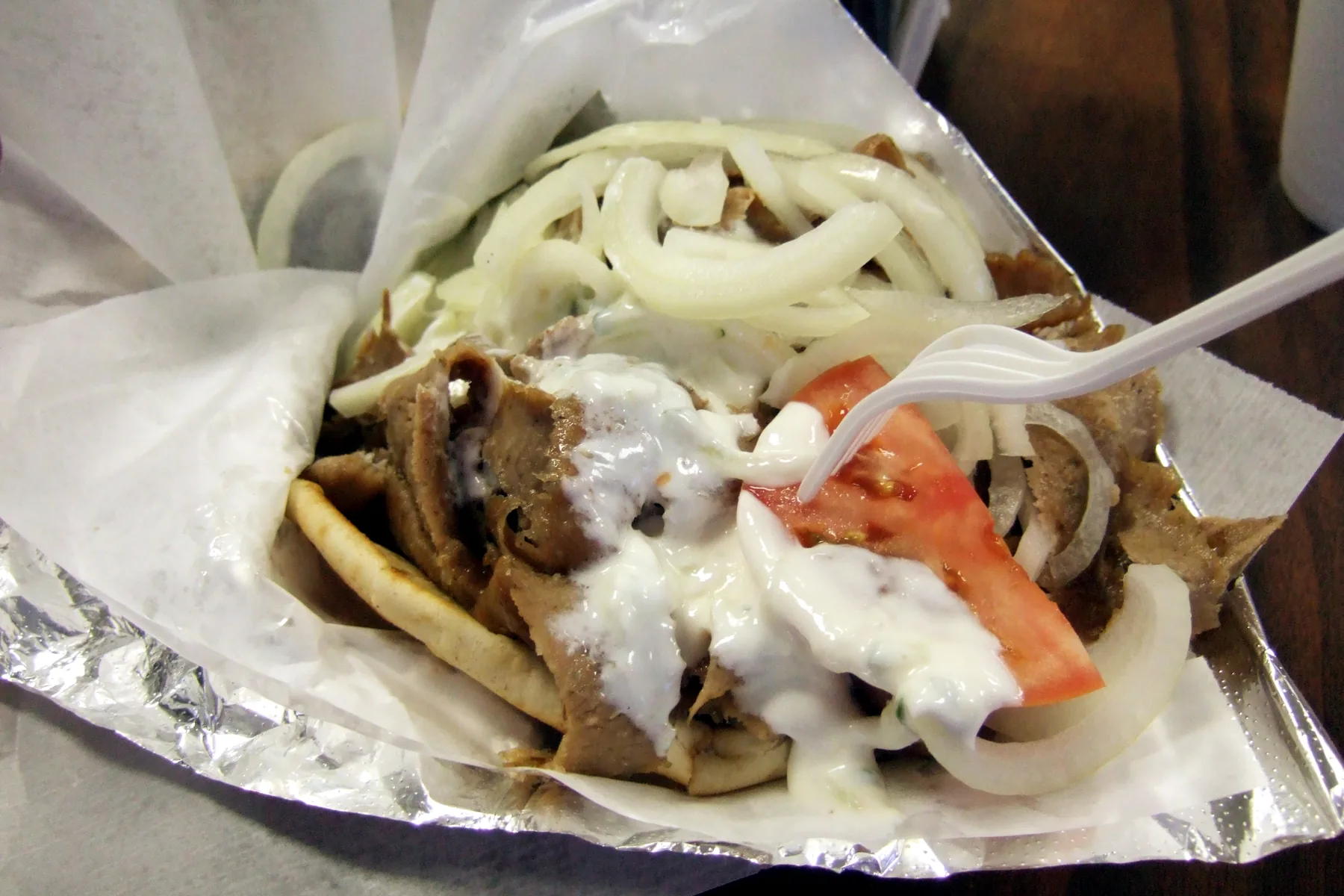 A gyro sandwich in soft pita with sliced meat, tomato, onion, and tzatziki