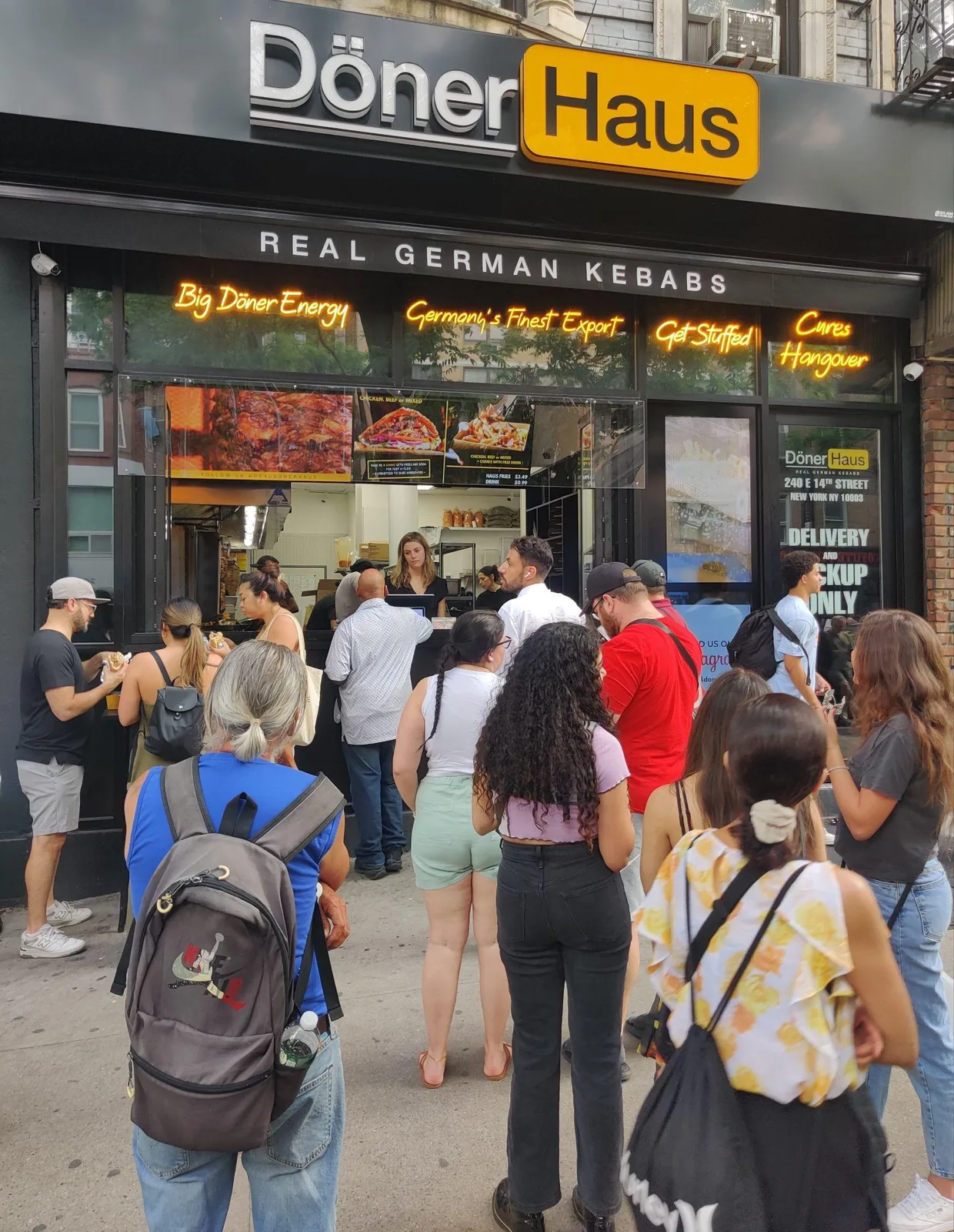 Customers queueing on the pavement outside a döner shop